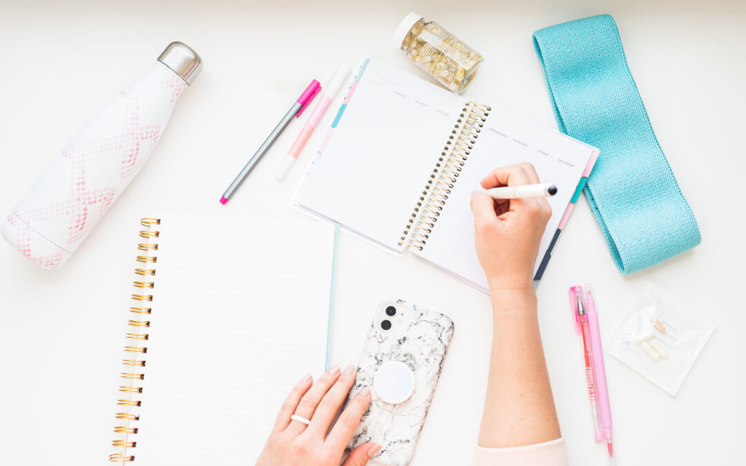 Discover the ultimate strategy for crafting compelling content that captivates your audience. Image of white woman's hands writing in journal and planner. Water bottle, vitamins and pens are in the image as well.